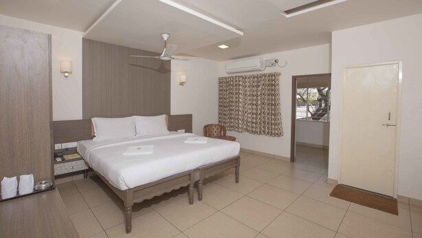 A hotel room with a large bed, a ceiling fan, an air conditioning unit, and a door leading to another room. - Hotel Sownthariyam (Palani)
