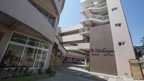 A multi-story hotel with a central atrium, balconies on each floor, and a clear sky. - Hotel Sownthariyam (Palani)