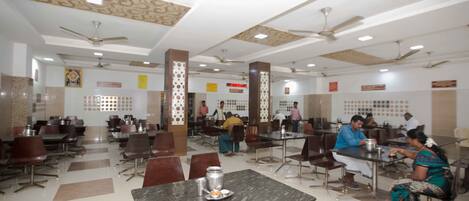 A spacious dining area with multiple tables and chairs, ceiling fans, and patterned wall designs.