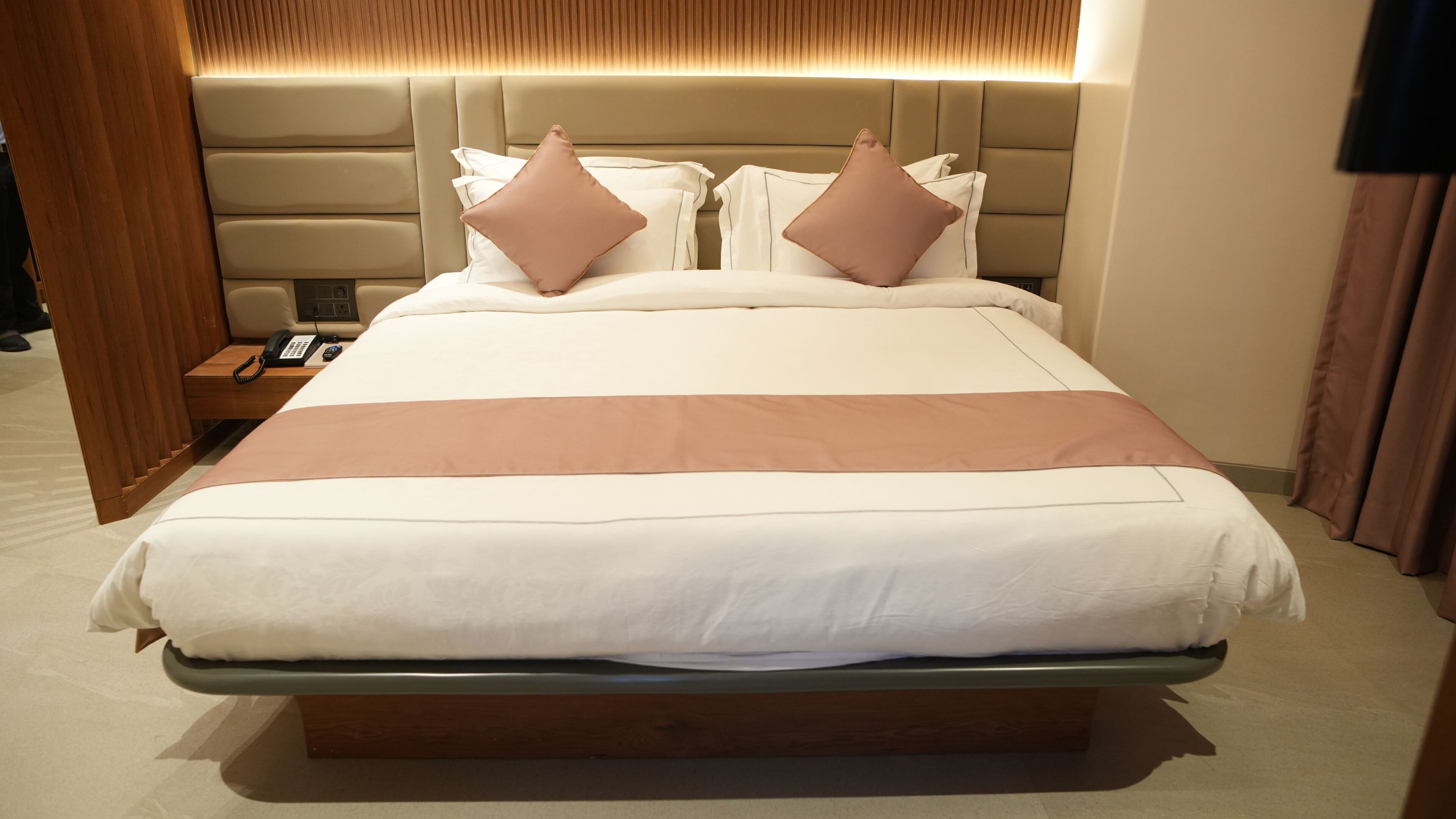 A neatly made bed with a headboard, a bedside phone, and a wooden nightstand.