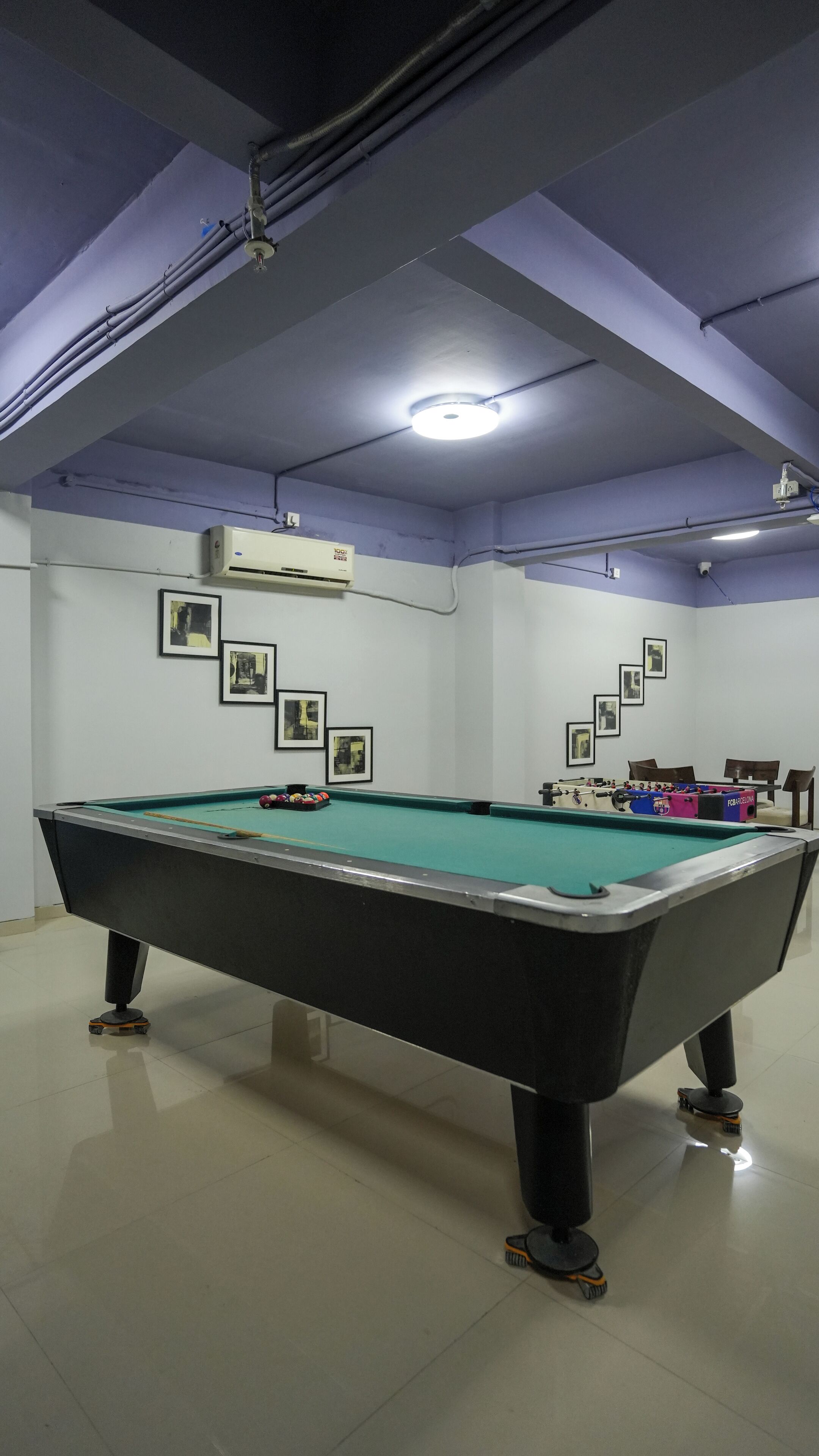 A pool table with a green felt surface, surrounded by a white wall with framed pictures.