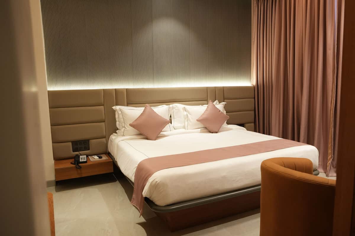 Ein modernes Hotelzimmer mit einem großen Bett, einem Nachttisch mit Telefon und Ladegerät sowie einem Holzstuhl.