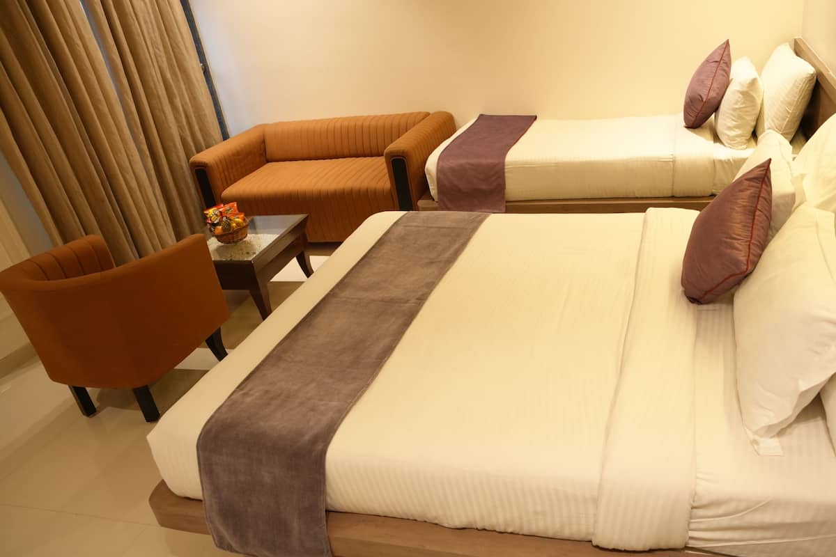 Ein Hotelzimmer mit einem großen Bett, zwei Sesseln, einem kleinen Tisch mit einer Obstkorb und einem Fenster mit Vorhängen.