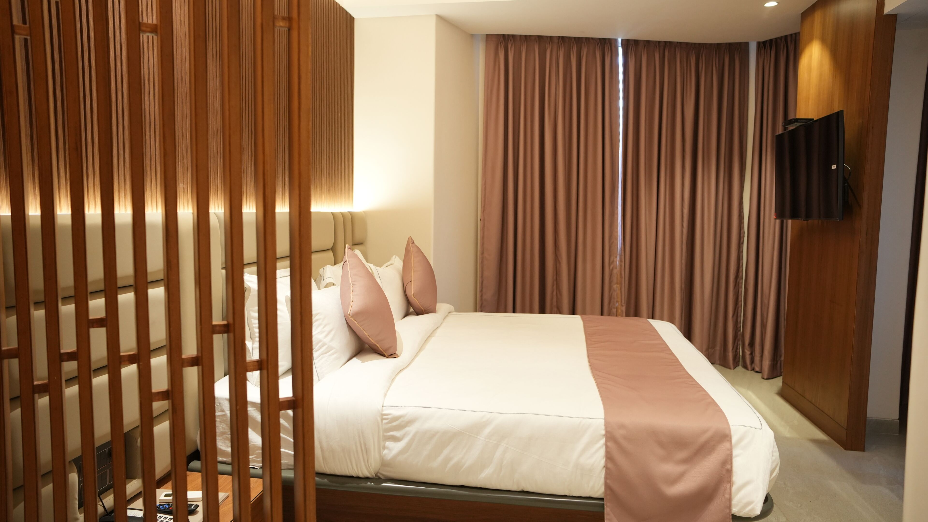 A hotel room with a bed, a TV mounted on the wall, and a wooden partition.