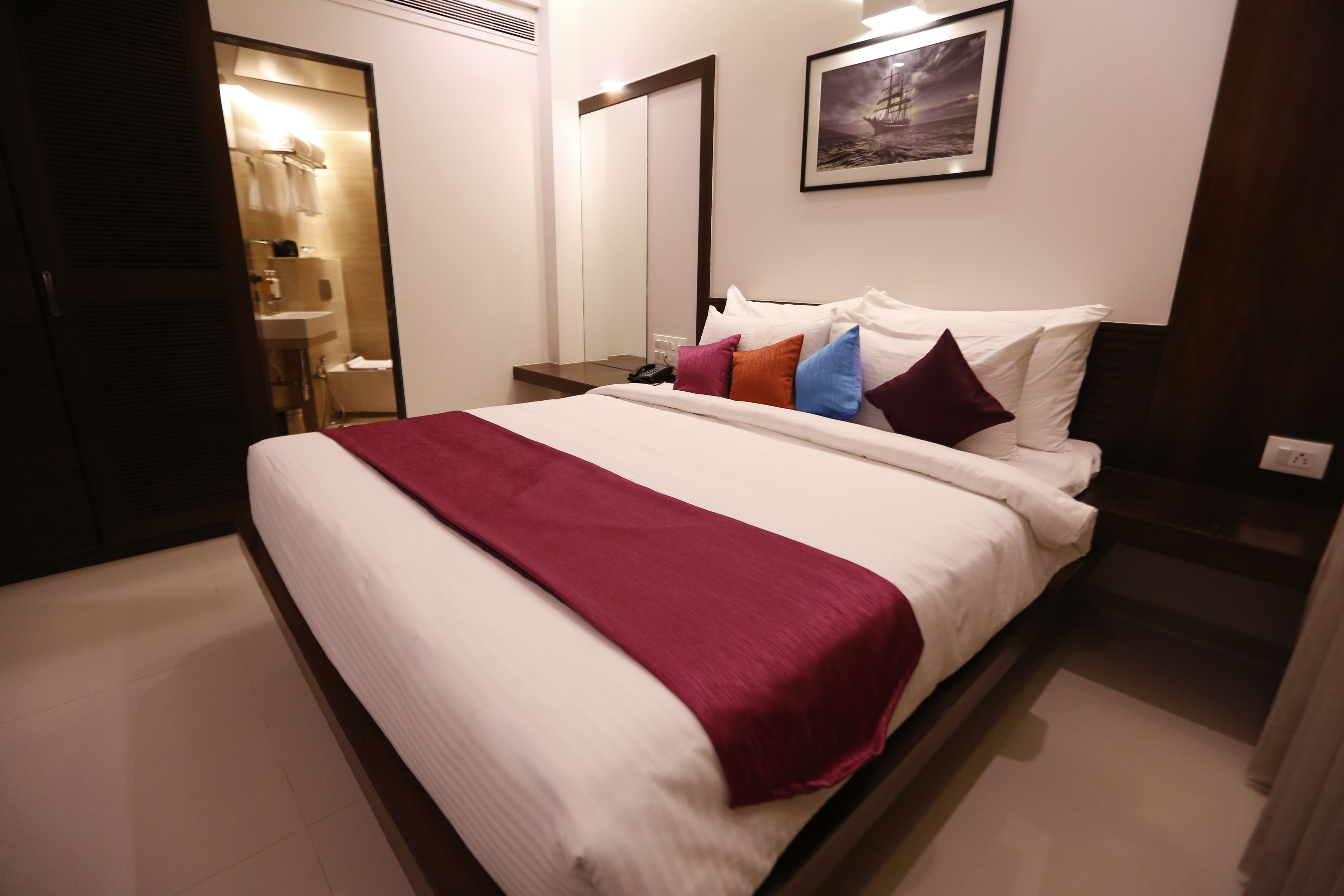 A hotel room with a large bed, a bedside table, a mirror, and a framed picture on the wall.