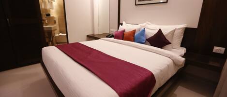 A hotel room with a large bed, a bedside table, a mirror, and a framed picture on the wall.