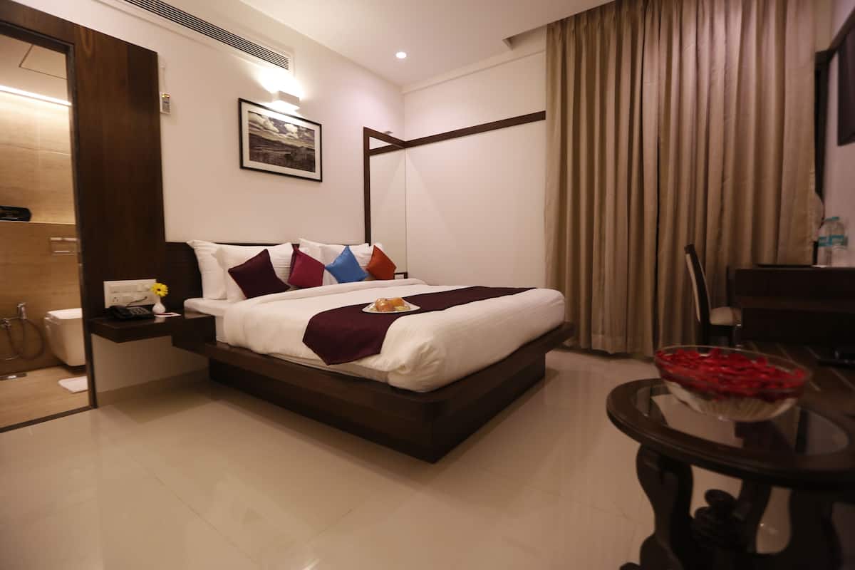 Ein Hotelzimmer mit einem großen Bett, einem Nachttisch mit Telefon und einer Vase, einem kleinen Tisch mit Obstschale und einem Badezimmer mit Toilette und Dusche.