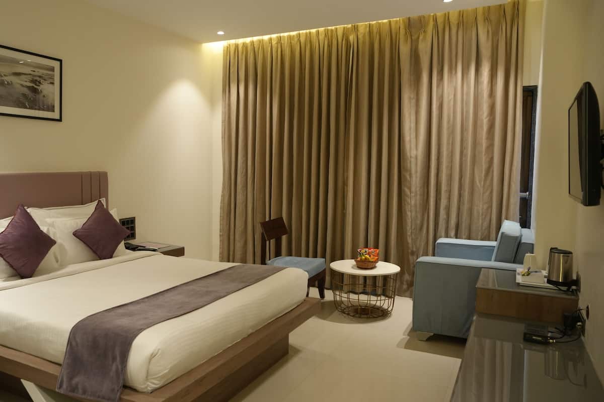 Ein Hotelzimmer mit Bett, Schreibtisch, Stuhl, kleinem Tisch und Vorhang.