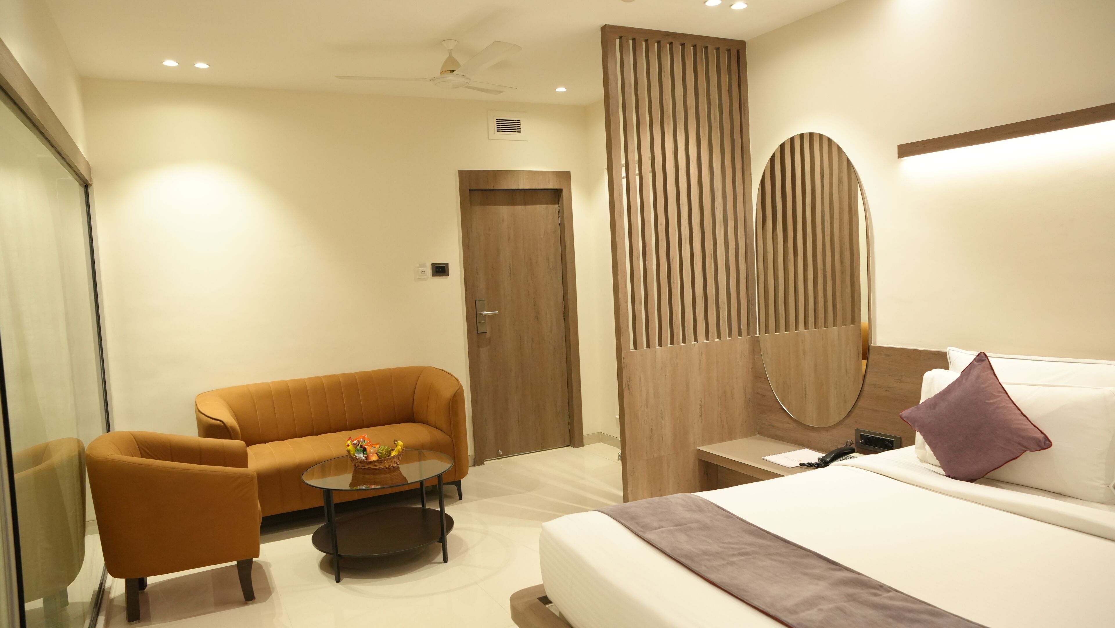 A modern hotel room with a sofa, a small round table, a bed with a pillow, and a wooden partition.