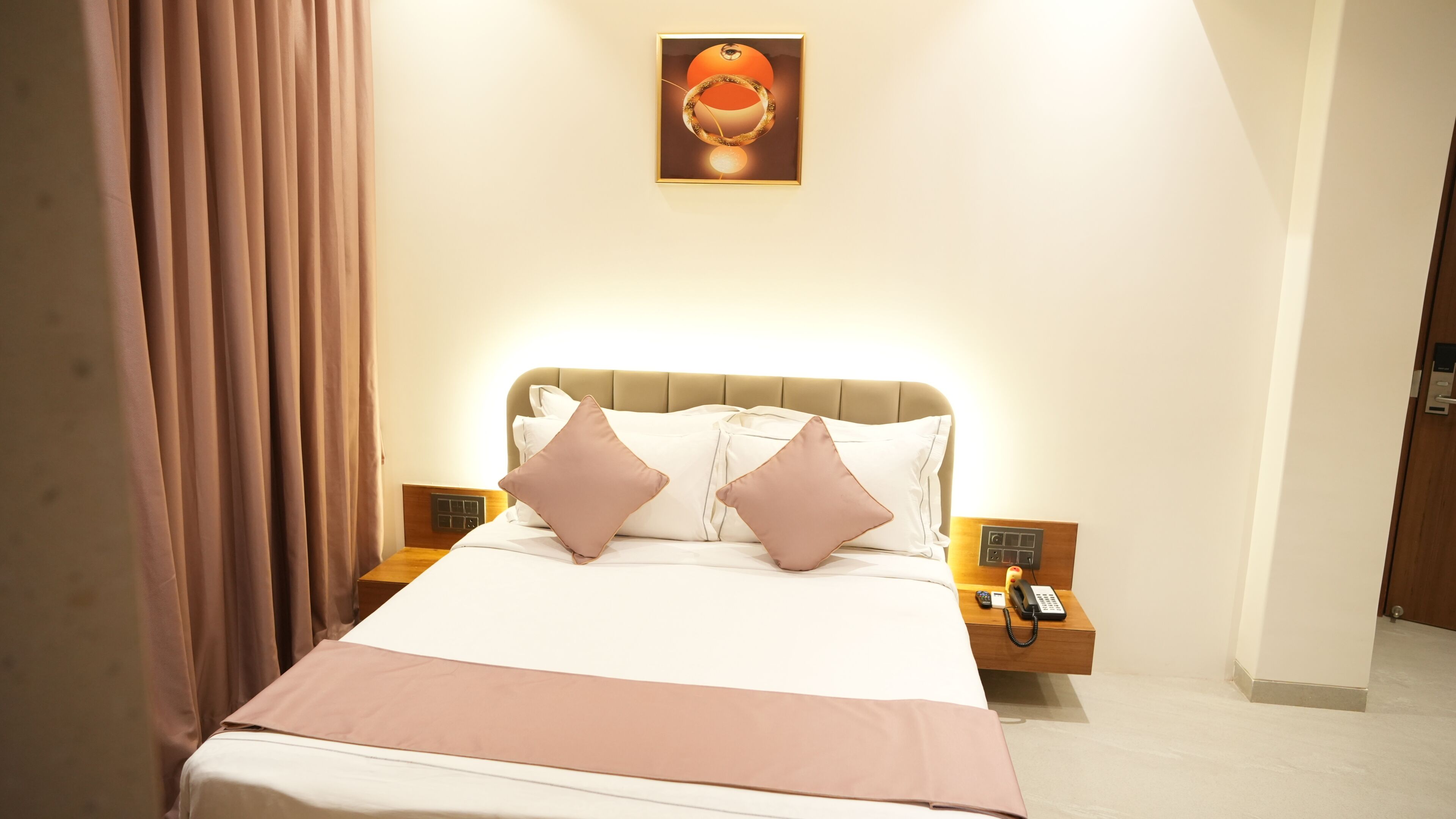 Une chambre d’hôtel comprenant un lit, deux tables de chevet, une commode, un téléphone fixé au mur et un tableau au-dessus du lit.