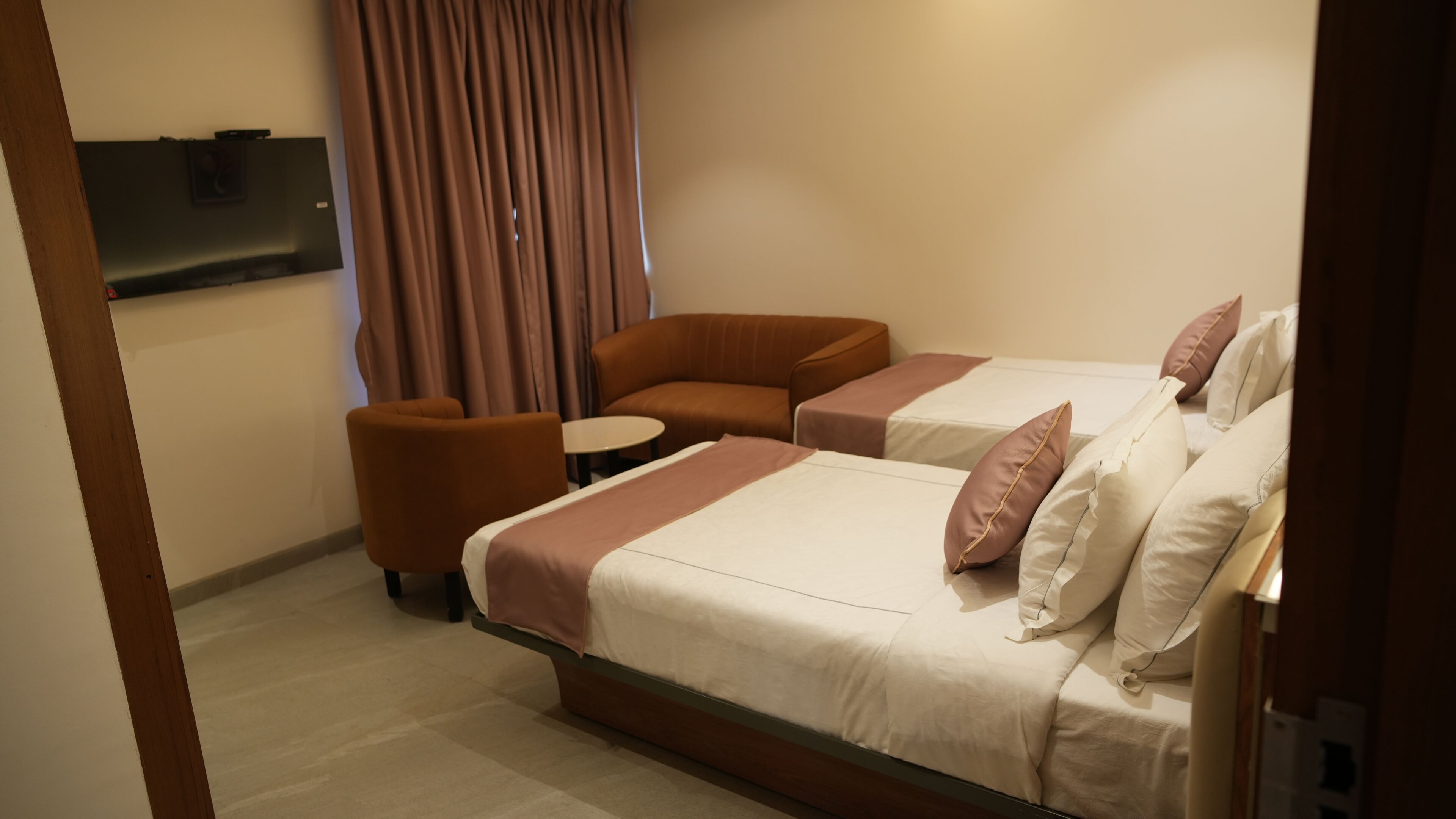 A hotel room with two beds, a sofa, a small table, and a TV mounted on the wall.