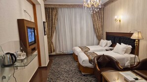 A hotel room with two beds, a TV, a chandelier, and a desk with a lamp. - Canary Beach Hotel (Yanbu)