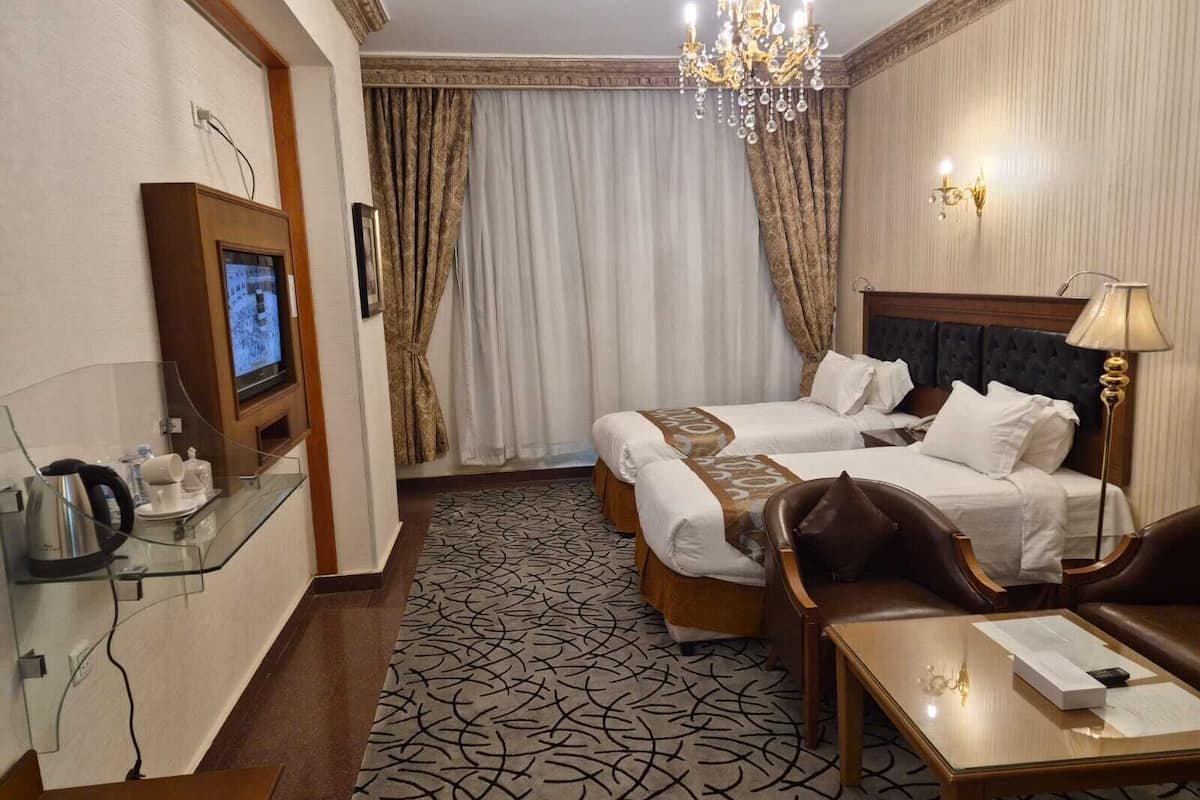 Habitación de hotel con dos camas, televisor, araña y escritorio con lámpara.