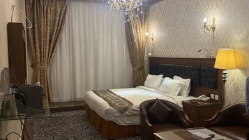 A hotel room with a large bed, a desk, a chair, a nightstand, a lamp, and a chandelier.