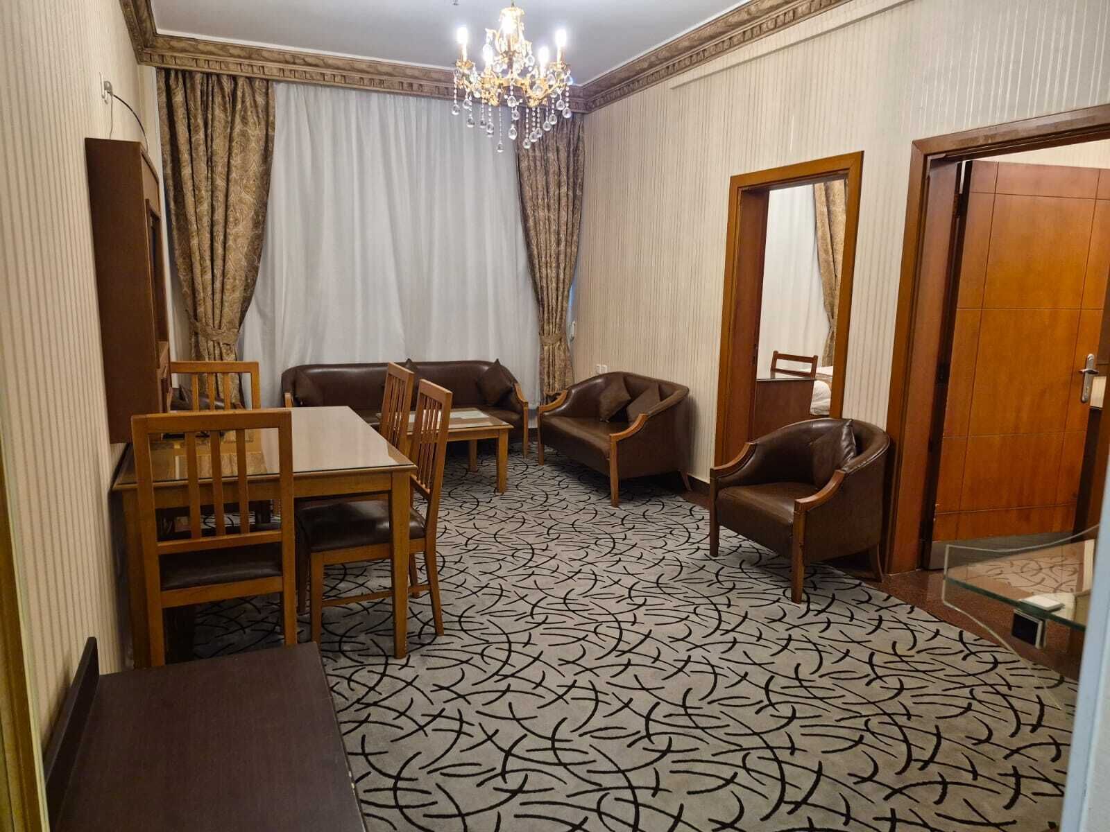 A hotel room with a dining table, two sofas, a chair, a mirror, and a patterned carpet.