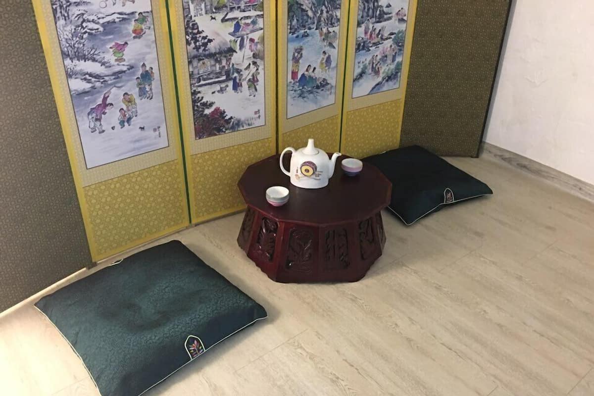 Une pièce avec une table ronde en bois, une théière blanche et deux coussins noirs.
