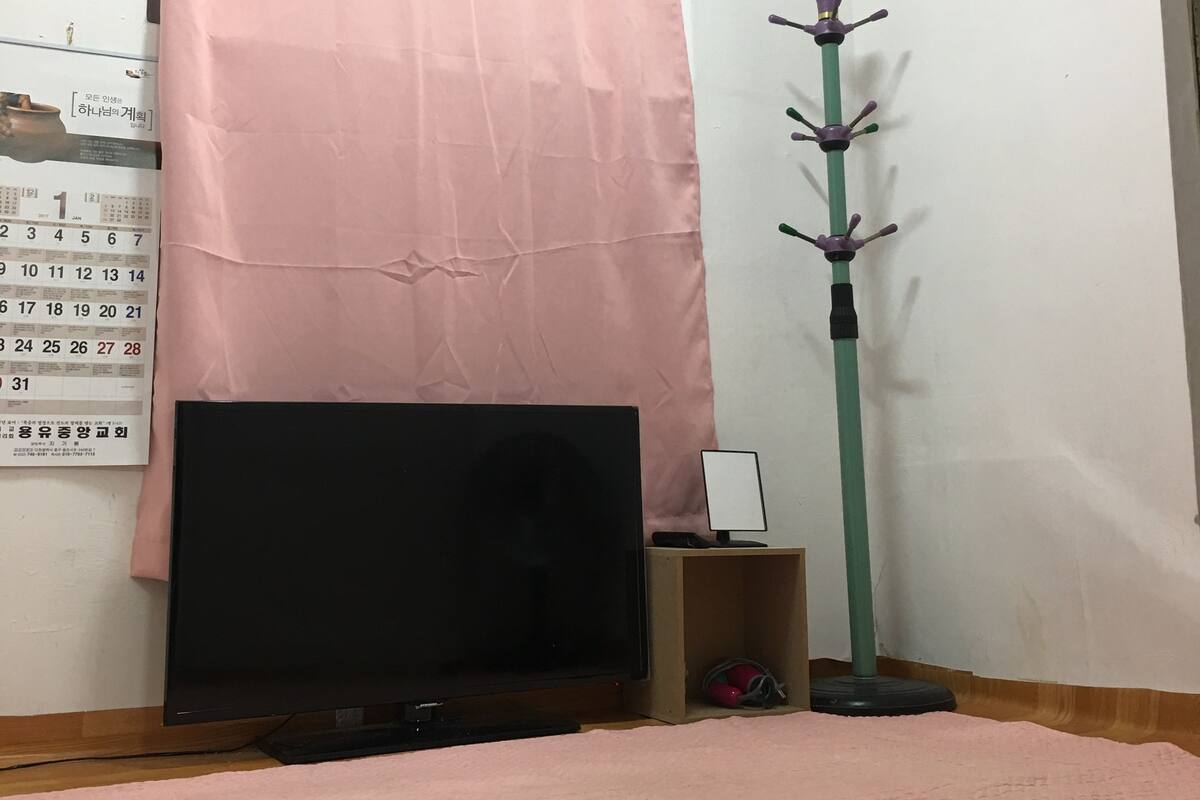 Une pièce avec une télévision, un rideau rose, un porte-manteau et un calendrier accroché au mur.