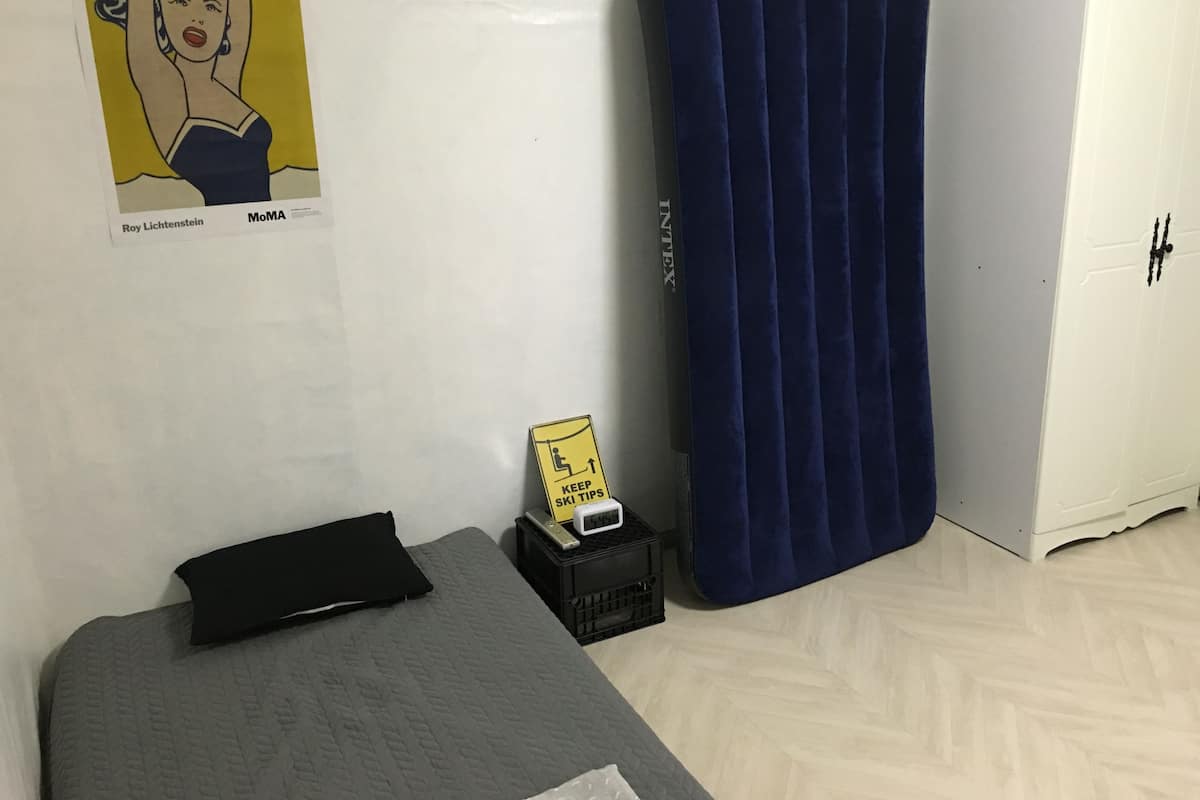Une pièce avec un lit, un rideau bleu, une armoire blanche et une affiche accrochée au mur.