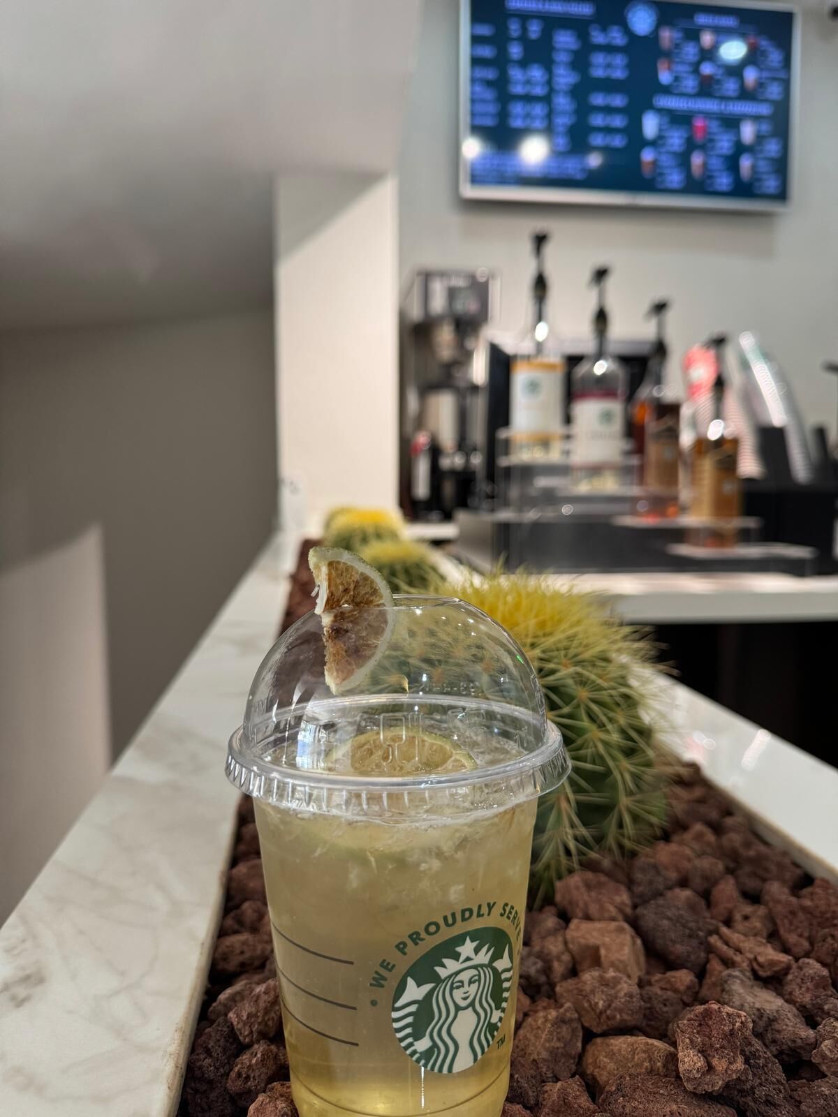 Una taza de Starbucks sobre una encimera de mármol, con un tablero de menú al fondo.