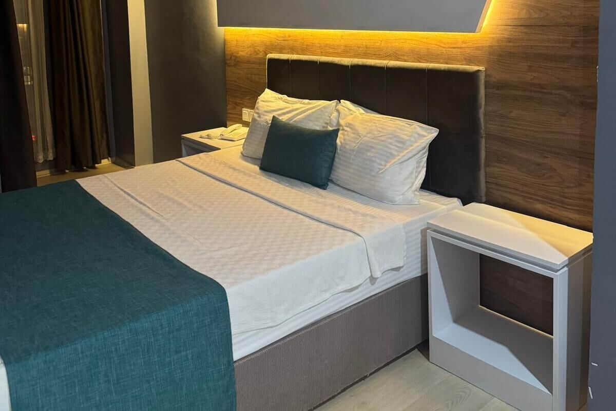 Una habitación de hotel moderna con una cama grande, mesitas de noche y un cabecero integrado.