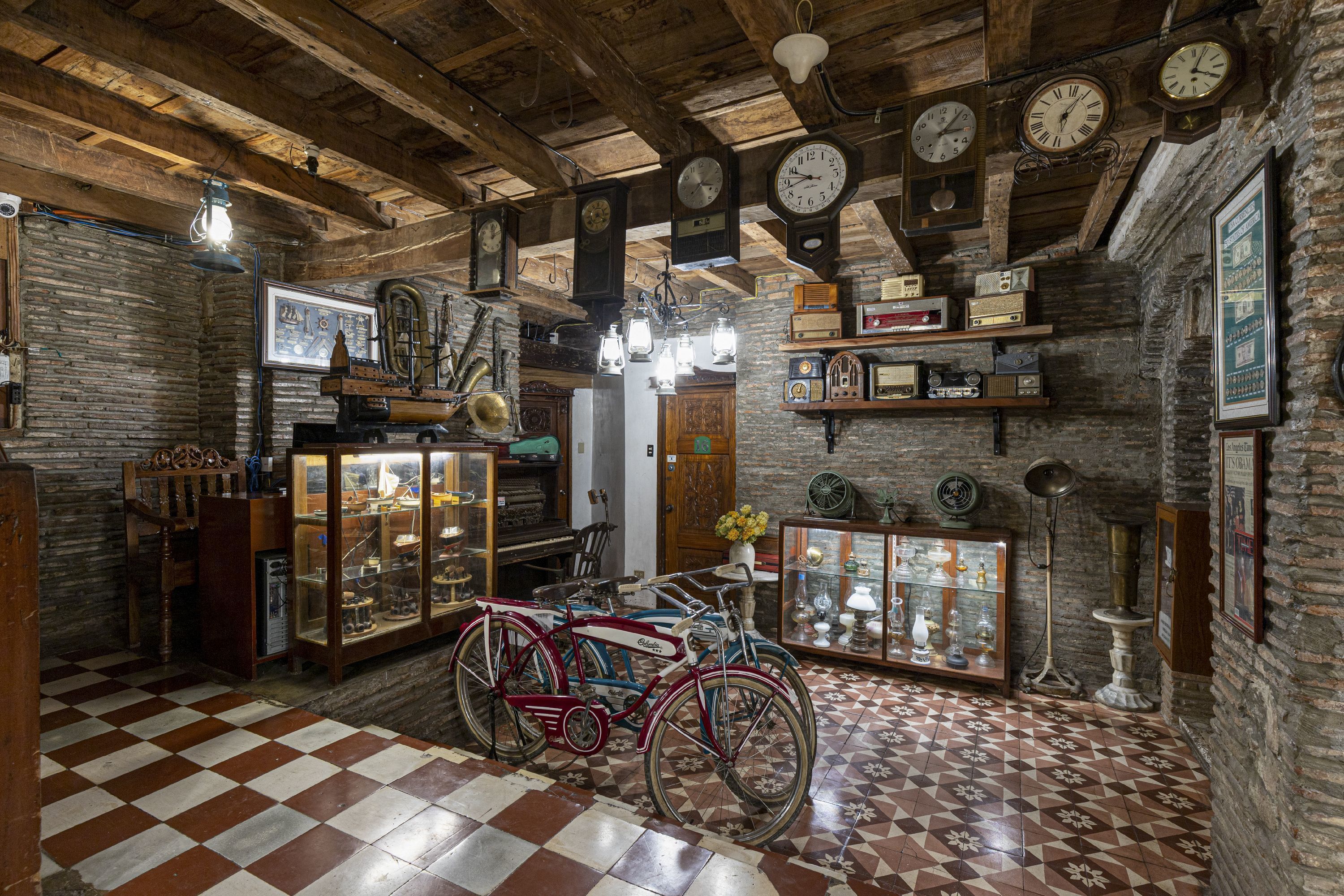 Quarto antigo com vigas de madeira, soalho xadrez e bicicletas antigas.