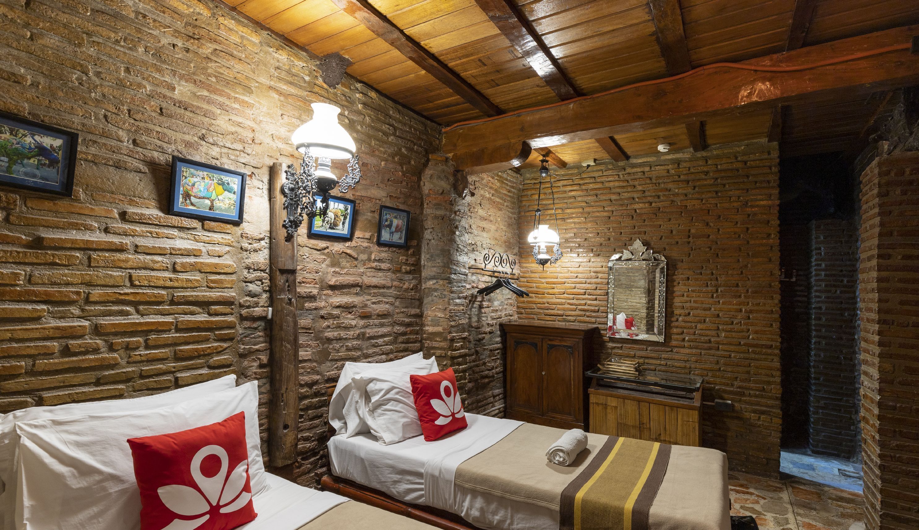 A rustic room with exposed brick walls, wooden beams, and a bed with white linens and a red pillow.