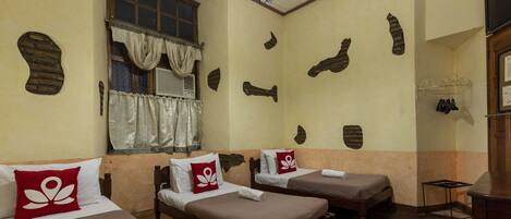 A room with two single beds, a window with curtains, a ceiling fan, and a brick wall decoration.