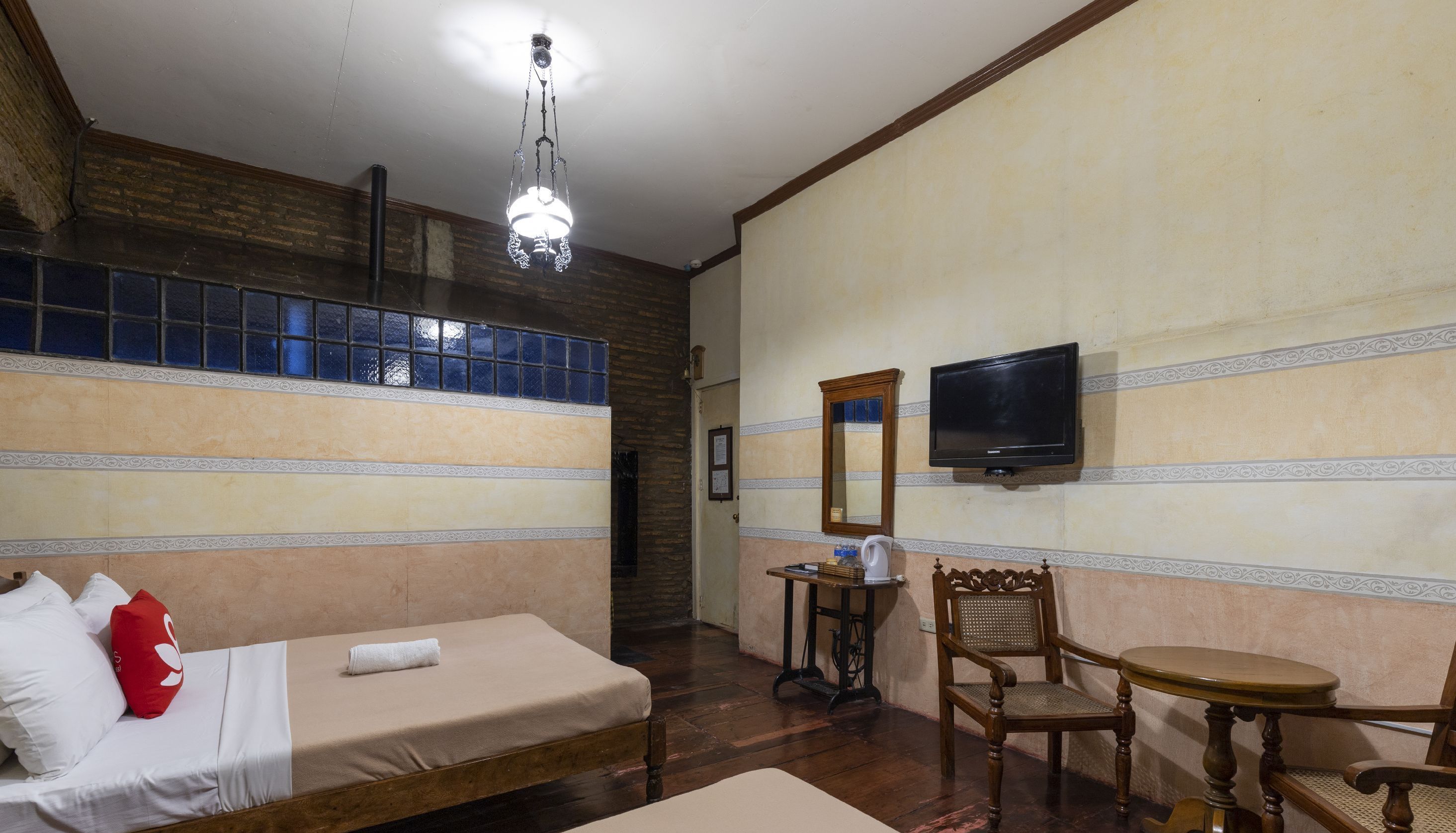 A hotel room with a bed, a chair, a table, a television, and a chandelier.