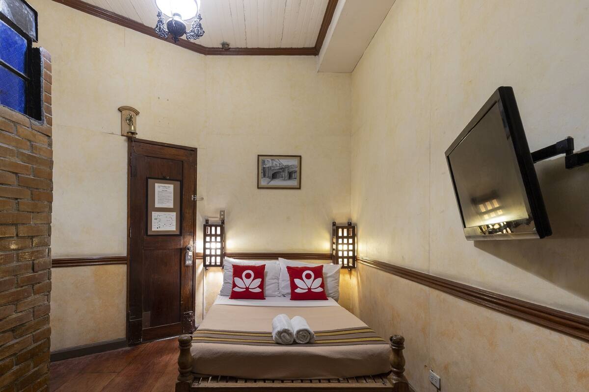A hotel room with a bed, a television, a door, and a brick wall.