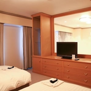 Una camera d'albergo con due letti, una TV su un comò in legno e un grande specchio.