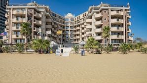 Un hotel de varios pisos con balcones, situado en una playa de arena.