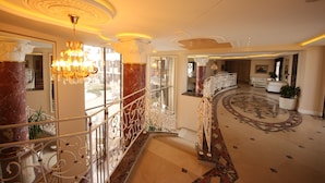 Un amplio vestíbulo de hotel con suelo de mármol, candelabros ornamentados y un diseño espacioso con balcón.