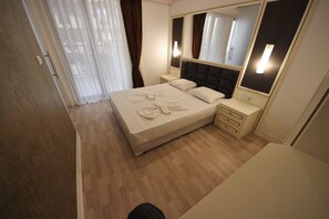 A modern hotel room with a large bed, bedside tables, a mirror, and a wooden floor. - Menada Golden Rainbow Apartments (Sunny Beach)
