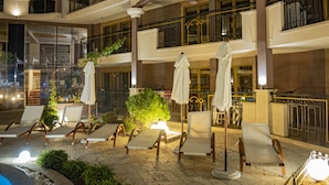 Un hall de hotel con varias sillas de descanso y sombrillas, una zona de piscina y una escalera que sube a los pisos superiores.