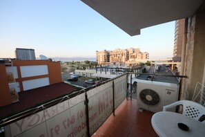A balcony with a view of a cityscape, a table, and a chair.
