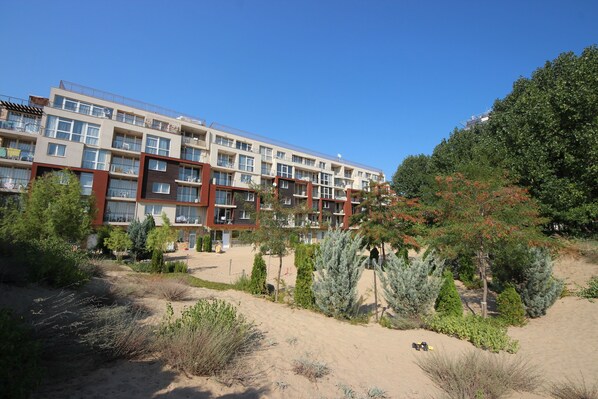 A multi-story residential building with balconies, surrounded by landscaped gardens and trees.