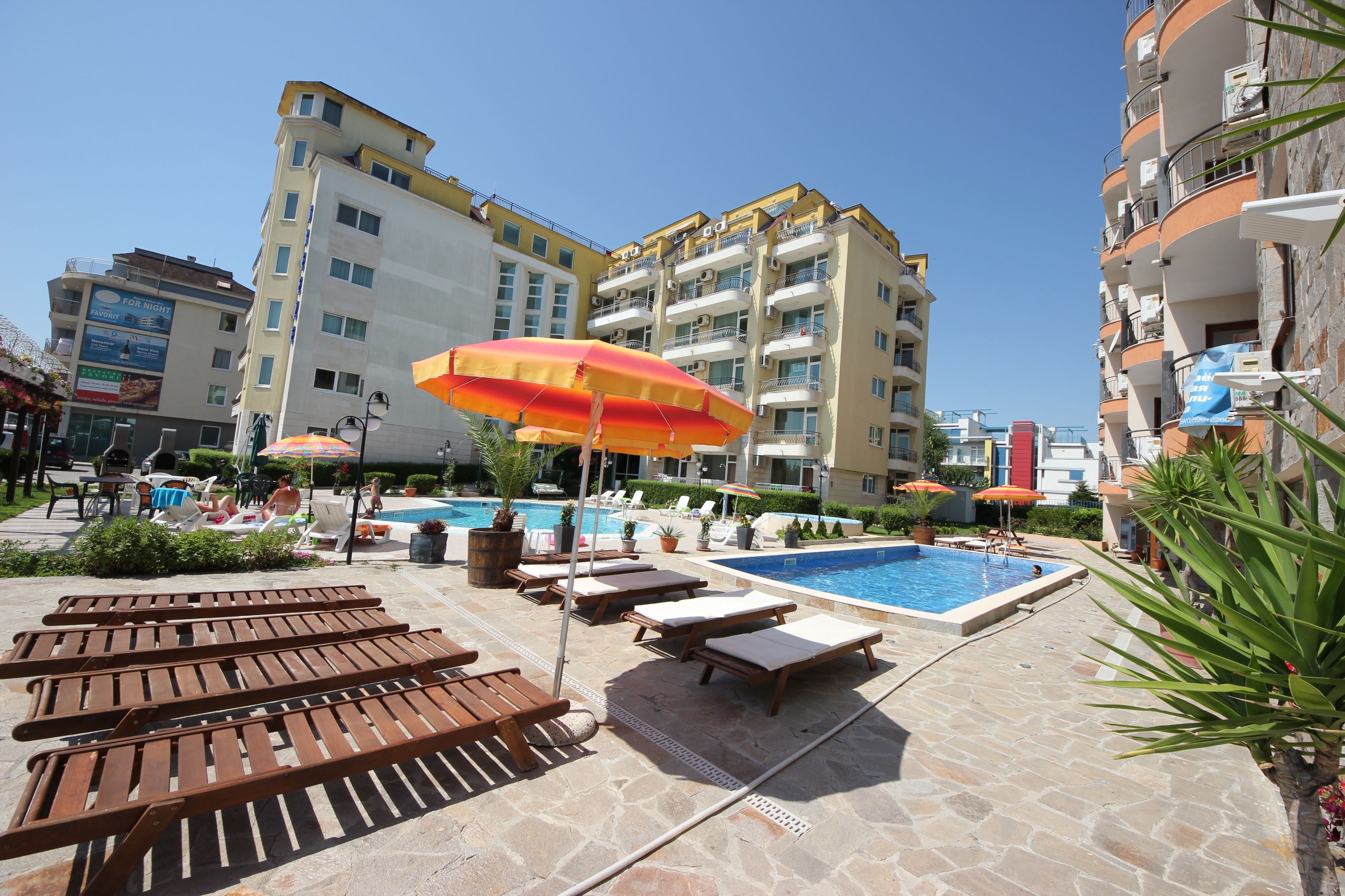 Zona junto a la piscina con tumbonas de madera, una piscina y sombrillas.