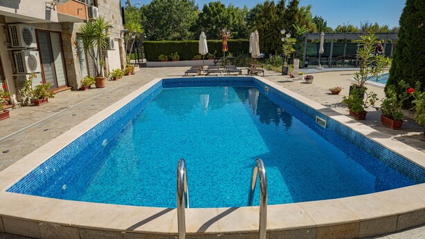 A rectangular swimming pool with clear blue water, surrounded by a stone deck and potted plants. - Menada Sea Regal Apartments (Sunny Beach)