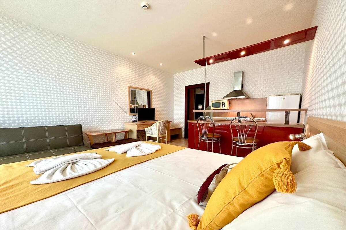Ein Hotelzimmer mit Bett, Schreibtisch, Stuhl, Mikrowelle und einer Küchenzeile.