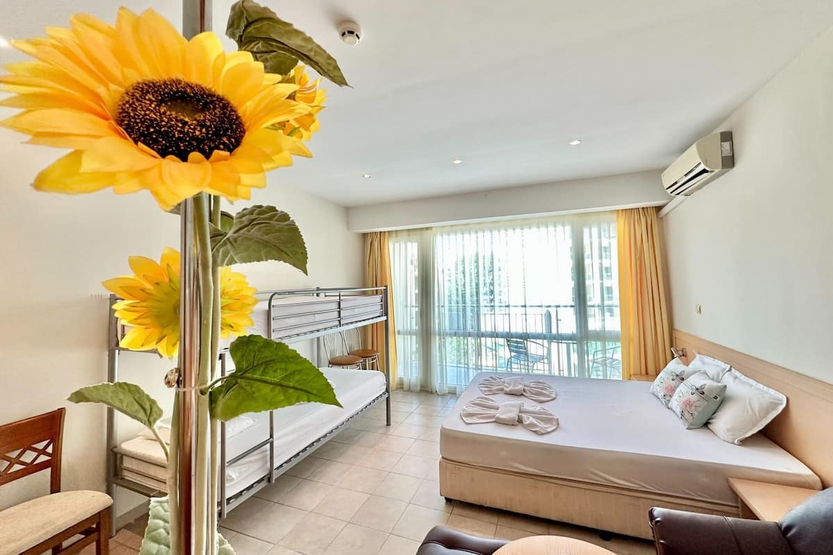 Ein Hotelzimmer mit Etagenbett, Schlafsofa, einem großen Fenster mit Vorhängen und einer Sonnenblumendekoration.