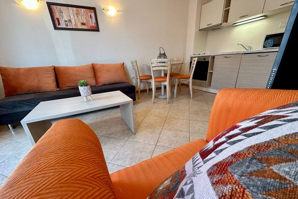 A modern living room with a sofa, chairs, a coffee table, and a kitchen area with cabinets and a sink.