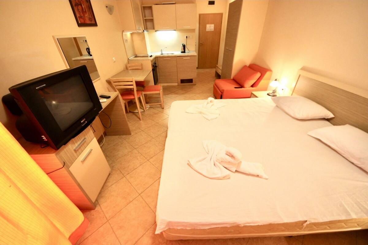 A hotel room with a bed, a desk, a chair, a television, and a kitchenette.