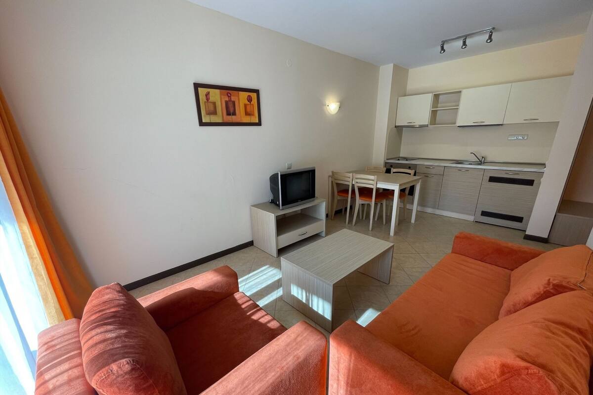 A modern living room with two orange sofas, a coffee table, a TV on a stand, and a dining area with a table and chairs.