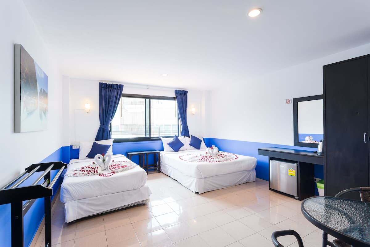 A hotel room with two beds, a small kitchenette, a dining table, and a view of the city.