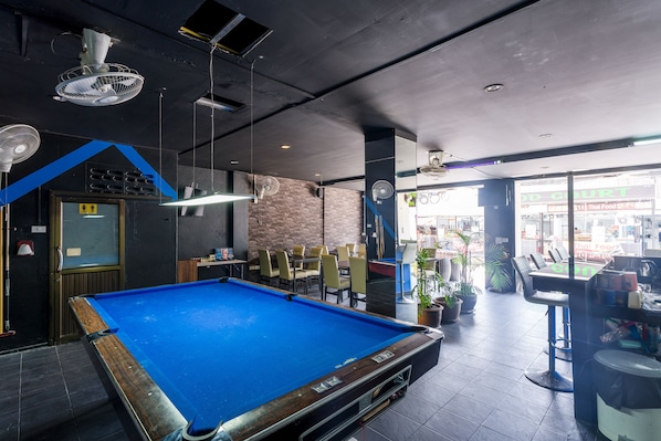 A pool table in a room with a brick wall, ceiling fans, and a view of a Thai restaurant.