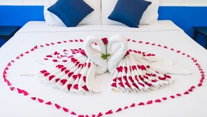 Una cama con ropa blanca, dos almohadas azules y una composición de toallas y pétalos de rosa en forma de corazón.