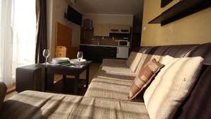 A living room with a sofa, a small table with a glass of wine, and a kitchen in the background. - Menada Grand Kamelia Apartments (Sunny Beach)