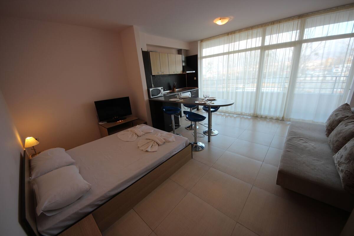 Ein Hotelzimmer mit Bett, Fernseher, Küchenzeile, Esstisch mit Stühlen und einer Couch.