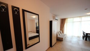 A hotel room with a bed, a large mirror, a wardrobe, a sofa, and a dining area with a table and chairs. - Menada Grand Kamelia Apartments (Sunny Beach)