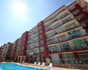 Un hôtel à plusieurs étages doté de balcons, d’une piscine et de chaises longues.